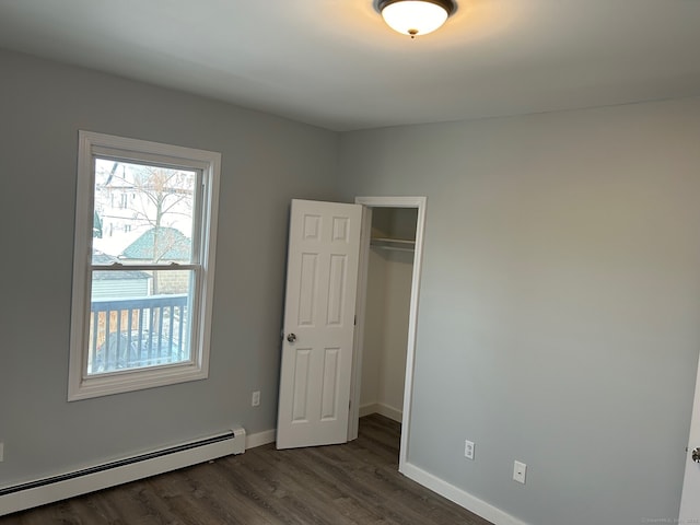unfurnished bedroom with baseboard heating, dark wood-style floors, baseboards, and a closet