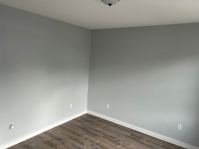 unfurnished room featuring baseboards and dark wood-type flooring
