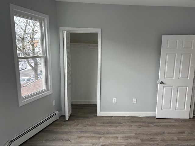 unfurnished bedroom featuring a baseboard heating unit, wood finished floors, a closet, and baseboards