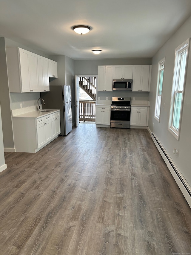 kitchen with stainless steel appliances, a baseboard heating unit, dark wood-style floors, and a sink