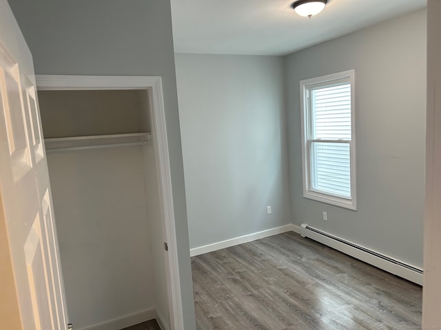 unfurnished bedroom with a baseboard heating unit, wood finished floors, a closet, and baseboards