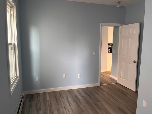 empty room with wood finished floors, baseboards, and baseboard heating