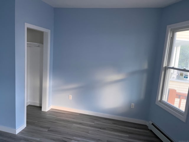 unfurnished room with a baseboard radiator, dark wood finished floors, and baseboards
