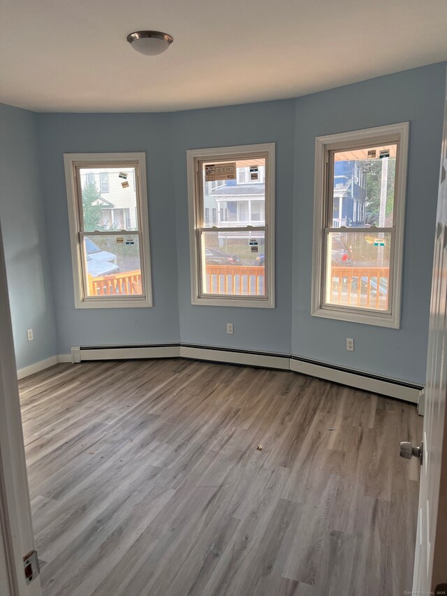 empty room featuring a baseboard radiator, wood finished floors, and baseboards