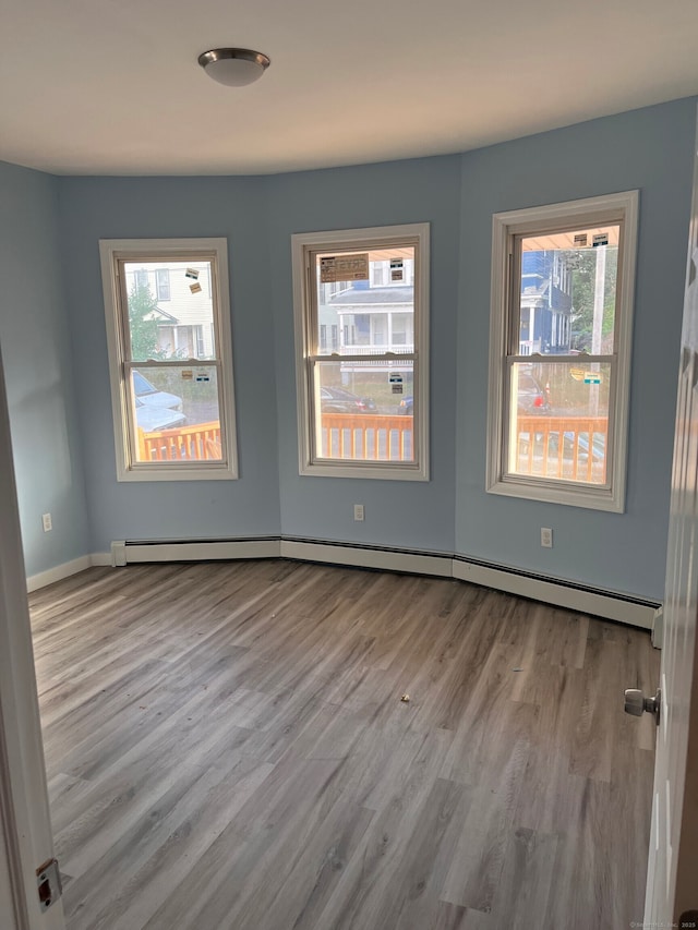 empty room featuring a baseboard radiator, wood finished floors, and baseboards
