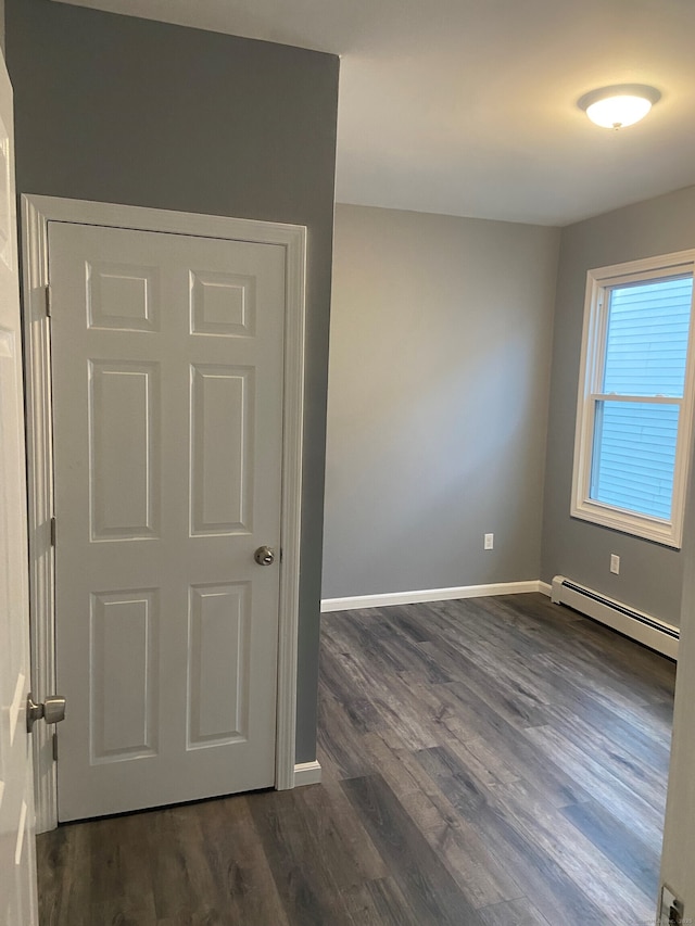 spare room with a baseboard heating unit, dark wood-type flooring, and baseboards