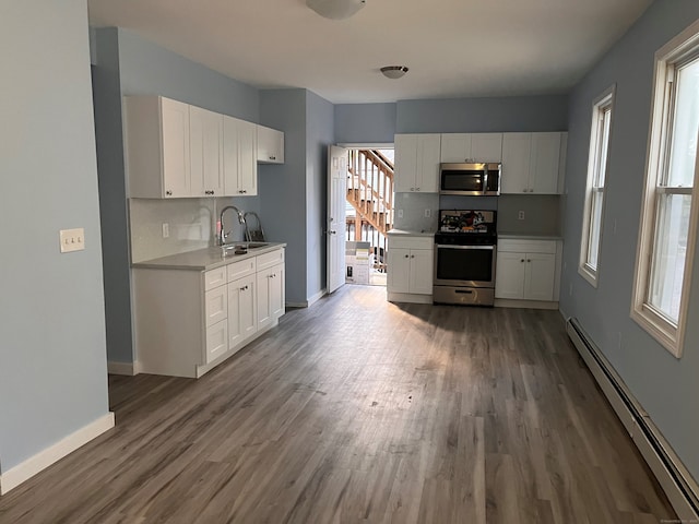 kitchen with stainless steel appliances, baseboard heating, a sink, wood finished floors, and light countertops