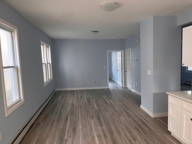 spare room featuring a baseboard heating unit, wood finished floors, baseboards, and healthy amount of natural light