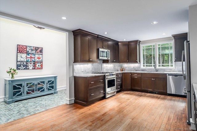 kitchen featuring appliances with stainless steel finishes, light wood finished floors, dark brown cabinetry, decorative backsplash, and a sink