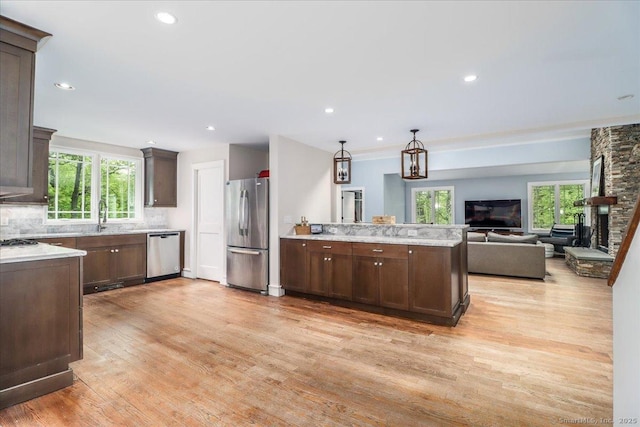 kitchen featuring stainless steel appliances, light wood-style floors, open floor plan, backsplash, and dark brown cabinets