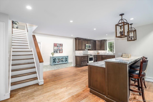 kitchen with stainless steel appliances, a peninsula, dark brown cabinets, light wood-style floors, and light stone countertops