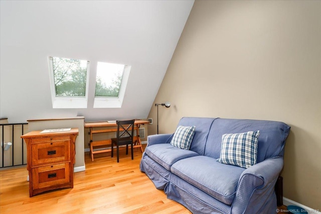 living area featuring light wood finished floors, a skylight, baseboards, and lofted ceiling
