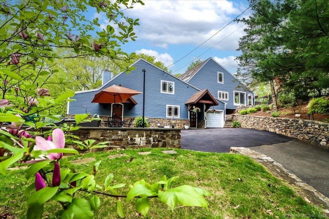 view of front of property with driveway, a chimney, an attached garage, and stone siding