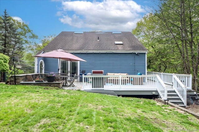 rear view of property with a lawn, a wooden deck, and roof with shingles