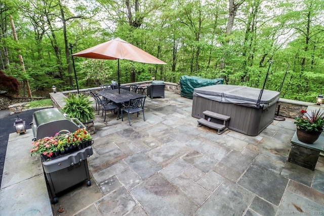 view of patio / terrace with a hot tub, outdoor dining area, and a wooded view