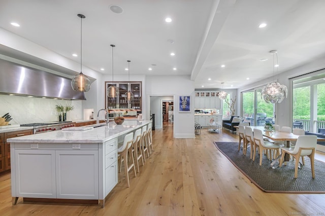 6 Spectacle Ln, Ridgefield, CT 06877 - kitchen featuring light wood-style flooring, light stone countertops, wall chimney range hood, a spacious island, and stainless steel gas stovetop