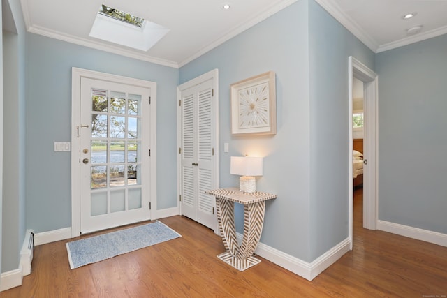 entrance foyer featuring a skylight, a baseboard heating unit, wood finished floors, baseboards, and ornamental molding