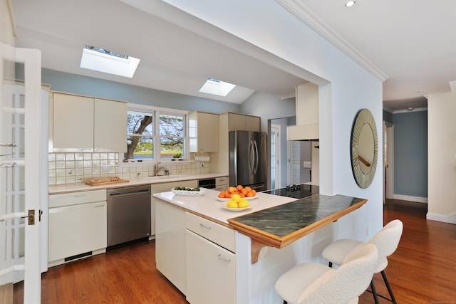 kitchen with appliances with stainless steel finishes, a skylight, a sink, ornamental molding, and a breakfast bar area