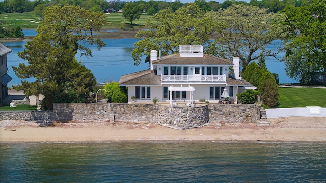 rear view of house with a balcony, a water view, a shingled roof, a patio area, and a chimney