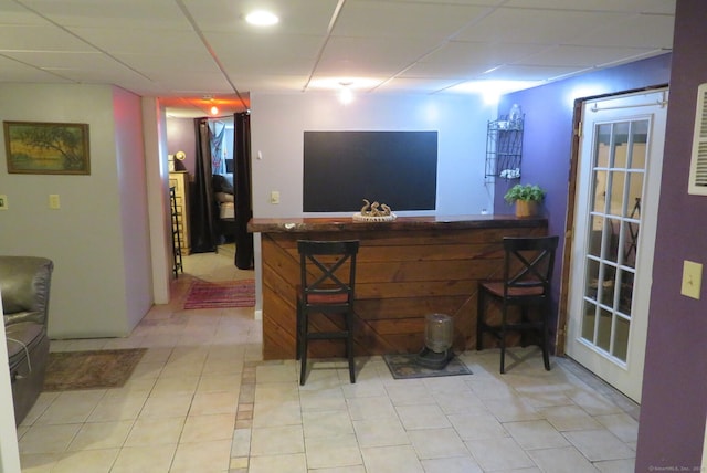 indoor dry bar with a paneled ceiling and light tile patterned floors