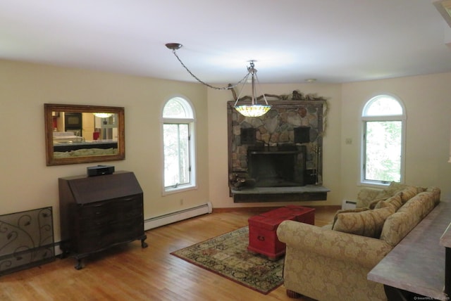 living room featuring a baseboard heating unit, plenty of natural light, wood finished floors, and a stone fireplace