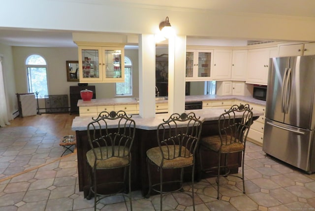 kitchen featuring freestanding refrigerator, black microwave, light countertops, a breakfast bar area, and glass insert cabinets