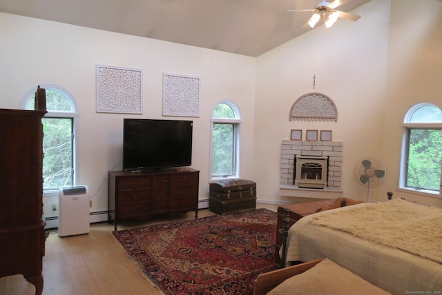 bedroom featuring high vaulted ceiling, wood finished floors, multiple windows, a baseboard heating unit, and a fireplace
