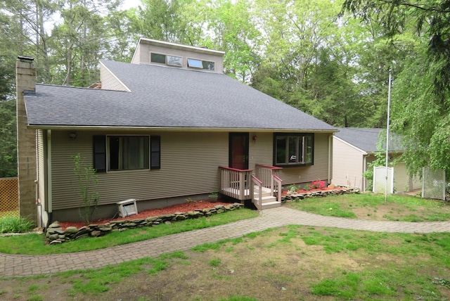 view of front of house with a shingled roof, a chimney, and a front yard