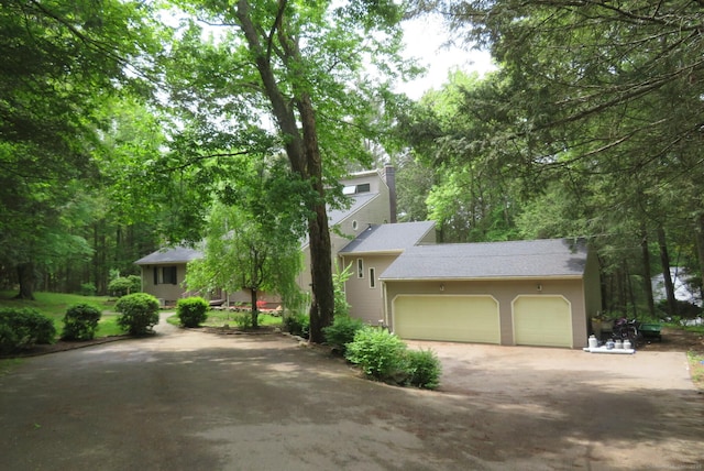 view of front of home with driveway, a chimney, a garage, and a shingled roof