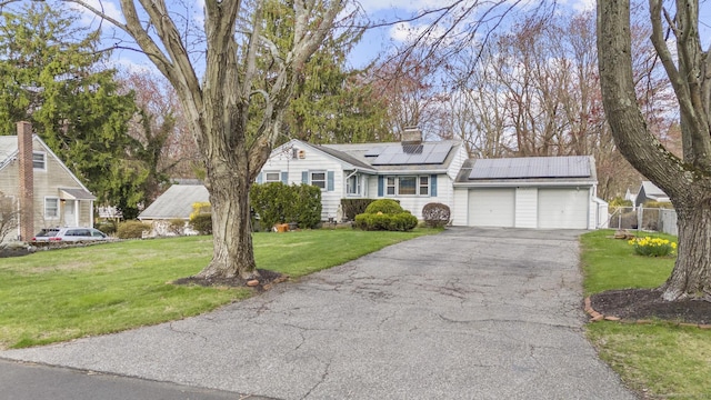 view of front facade featuring an attached garage, solar panels, a chimney, and asphalt driveway