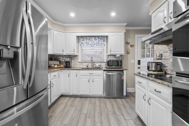 kitchen featuring appliances with stainless steel finishes, a sink, ornamental molding, backsplash, and light stone countertops