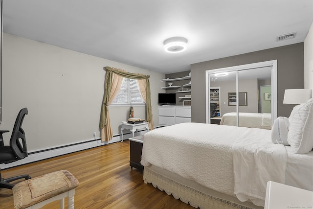 bedroom with wood finished floors, a closet, and baseboard heating