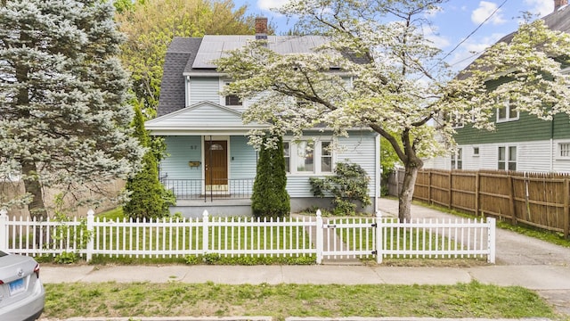 view of front facade featuring covered porch, solar panels, a chimney, and roof with shingles