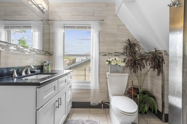 half bathroom with toilet, tile walls, tile patterned floors, vanity, and healthy amount of natural light