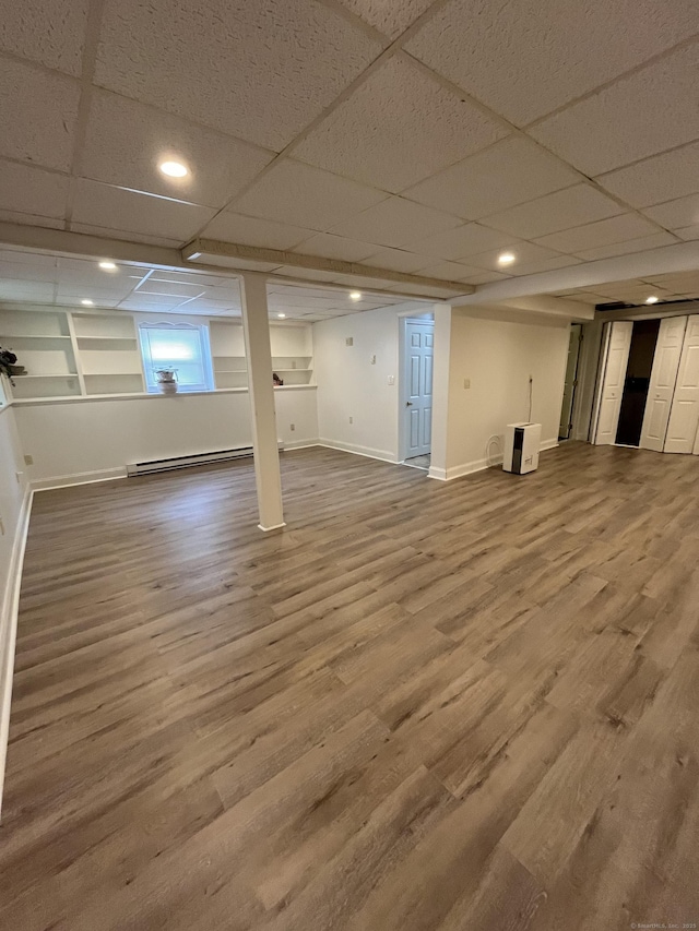 below grade area with baseboard heating, wood finished floors, baseboards, a drop ceiling, and recessed lighting