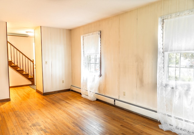 empty room with a baseboard heating unit, wood-type flooring, stairway, and baseboards