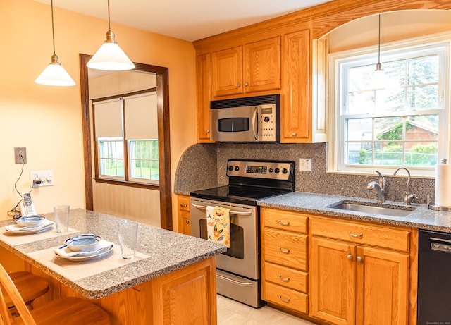 kitchen featuring appliances with stainless steel finishes, a sink, a kitchen bar, tasteful backsplash, and pendant lighting
