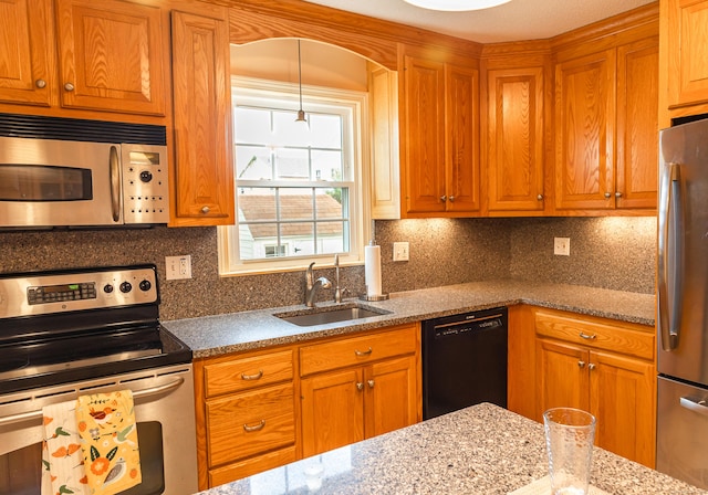 kitchen featuring appliances with stainless steel finishes, a sink, decorative backsplash, and brown cabinetry