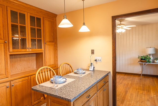 kitchen with brown cabinets, light wood-style floors, glass insert cabinets, ceiling fan, and decorative light fixtures