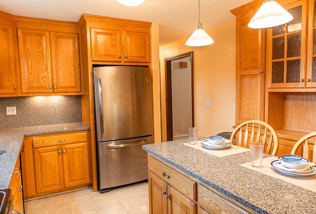 kitchen featuring freestanding refrigerator, brown cabinets, decorative light fixtures, and glass insert cabinets