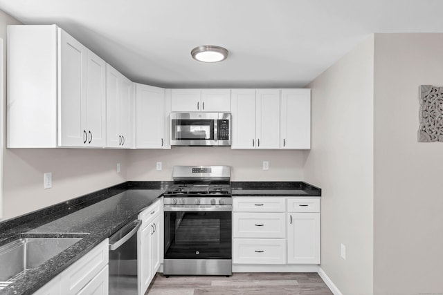 kitchen with appliances with stainless steel finishes, light wood-type flooring, white cabinets, dark stone counters, and a sink