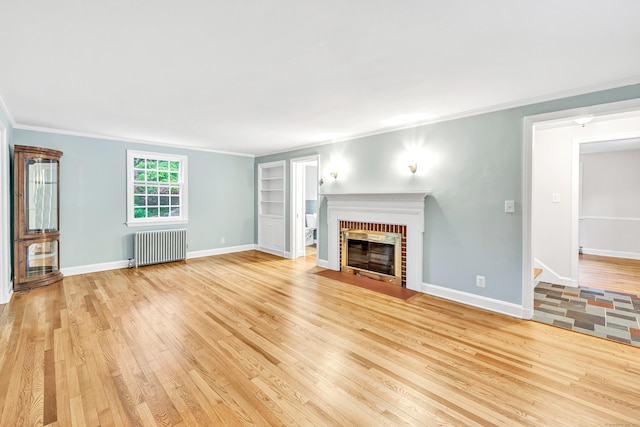 unfurnished living room featuring radiator, light wood-type flooring, ornamental molding, baseboards, and a fireplace