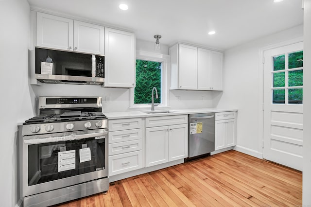kitchen featuring appliances with stainless steel finishes, a sink, light wood-style floors, white cabinets, and light countertops