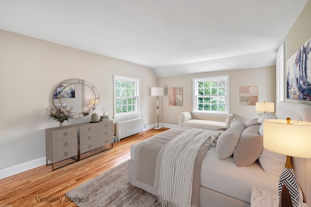 bedroom with radiator heating unit, wood finished floors, multiple windows, baseboards, and vaulted ceiling