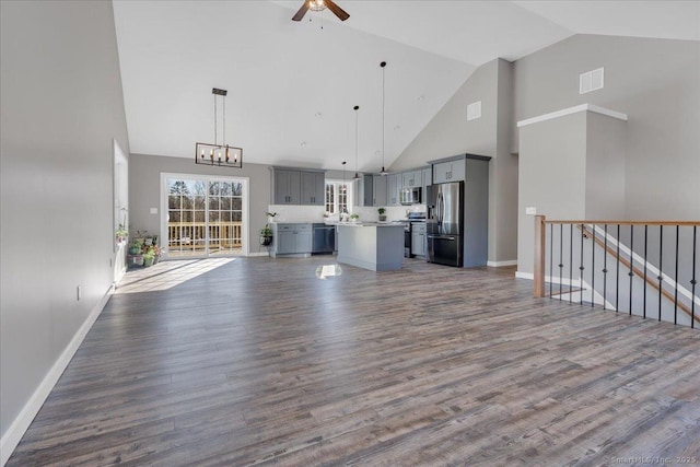 unfurnished living room with high vaulted ceiling, ceiling fan, a chandelier, dark wood-type flooring, and baseboards
