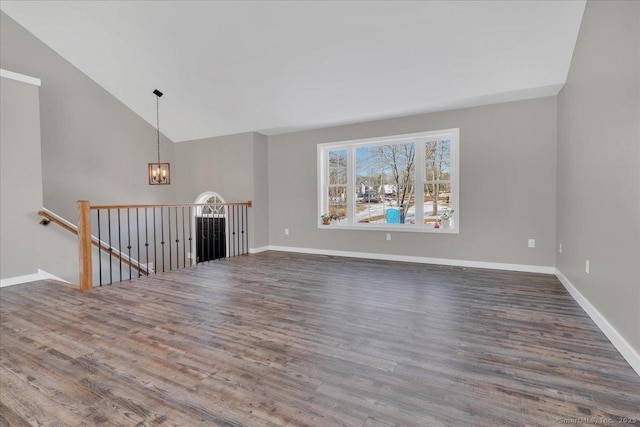 unfurnished living room featuring lofted ceiling, wood finished floors, a chandelier, and baseboards