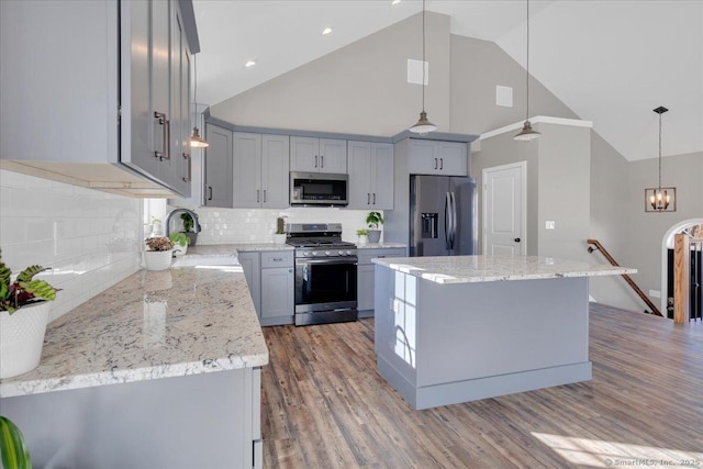 kitchen with appliances with stainless steel finishes, a sink, gray cabinets, a center island, and high vaulted ceiling