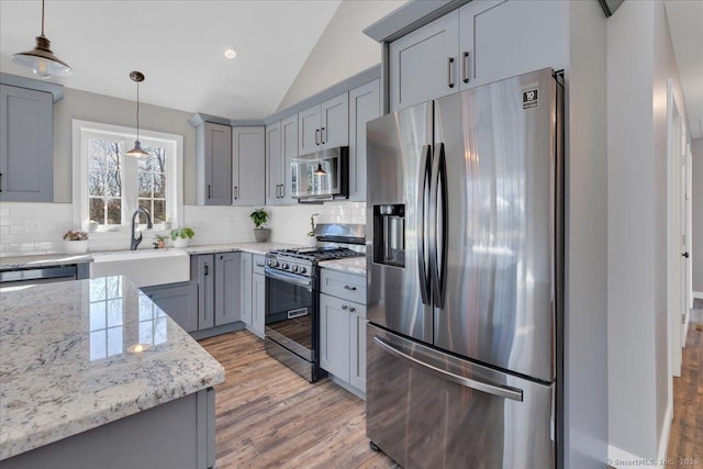kitchen featuring appliances with stainless steel finishes, gray cabinets, vaulted ceiling, backsplash, and light wood-style floors