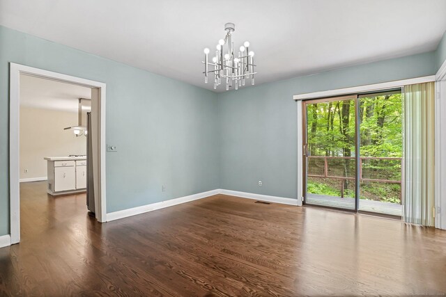 unfurnished room featuring a chandelier, dark wood-type flooring, and baseboards