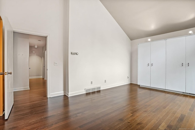 unfurnished bedroom featuring high vaulted ceiling, dark wood finished floors, baseboards, and a closet